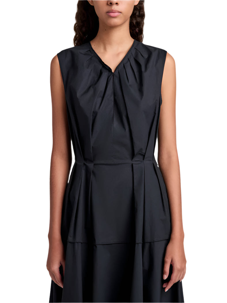 A woman wearing the Proenza Schouler White Label Kailey Dress Stretch Poplin, a sleeveless black fit-and-flare style with pleated neckline and waist, stands against a white background.