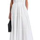 A woman wears the Kailey Dress Stretch Poplin by Proenza Schouler White Label—a sleeveless white V-neck pleated dress—paired with black strappy sandals and a black clutch.