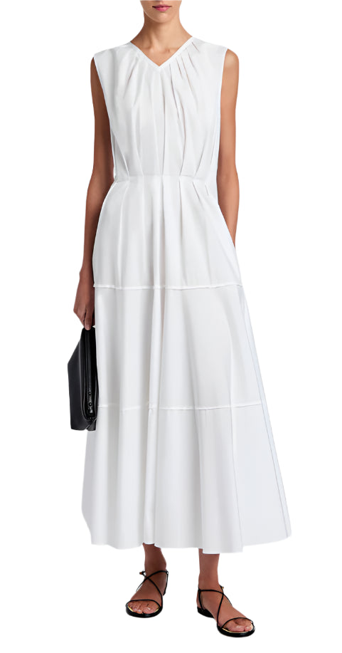 A woman wears the Kailey Dress Stretch Poplin by Proenza Schouler White Label—a sleeveless white V-neck pleated dress—paired with black strappy sandals and a black clutch.