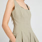 A person wears the Shelby Dress by Proenza Schouler White Label—a sleeveless, light beige fit-and-flare style with pleats, pockets, and a square neckline—standing against a plain light background.