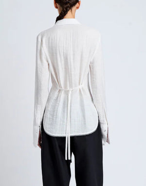A person is seen from behind wearing a relaxed-fit, long-sleeve white Cami Shirt Crinkle Viscose by Proenza Schouler White Label, tied at the waist, with black pants against a plain light background.