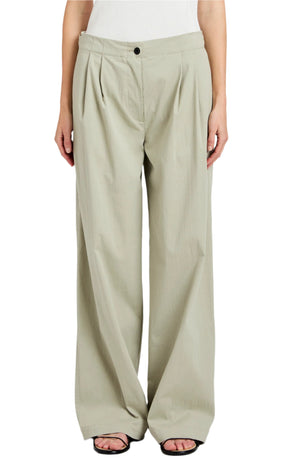 A person wears the Proenza Schouler White Label Romina Pant—loose-fitting, high-waisted, light beige cotton pants with a wide-leg silhouette, front pleats, black button closure—paired with open-toe black sandals.