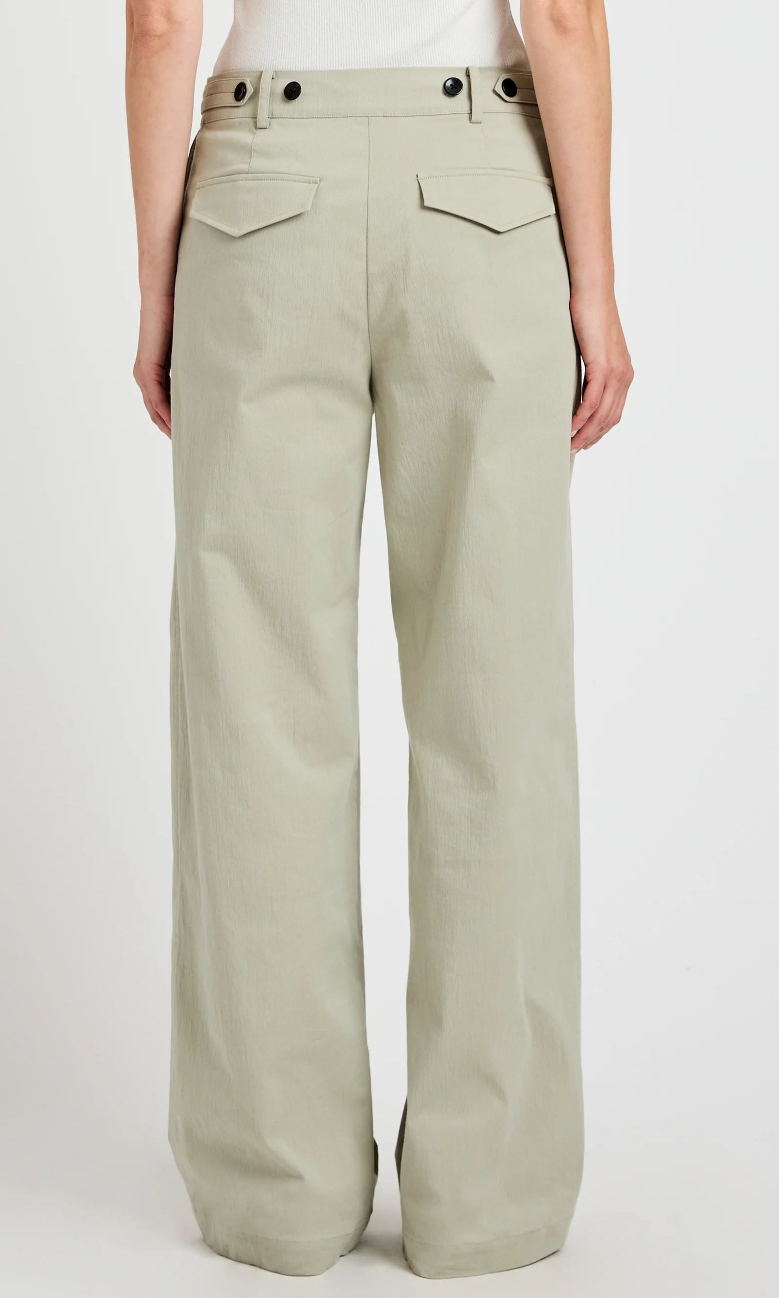 Model wears the Romina Pant by Proenza Schouler White Label, a high-waisted, wide-leg cotton style in light khaki with flap back pockets and black buttons, shown from the back.