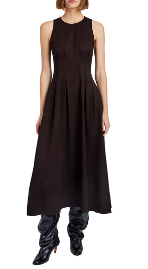 A woman wearing the Bronwyn Merino Wool Twill Dress by Proenza Schouler White Label— a sleeveless, ankle-length black A-line dress with a fitted bodice, flared skirt, and subtle pleat tucks—paired with shiny black boots.