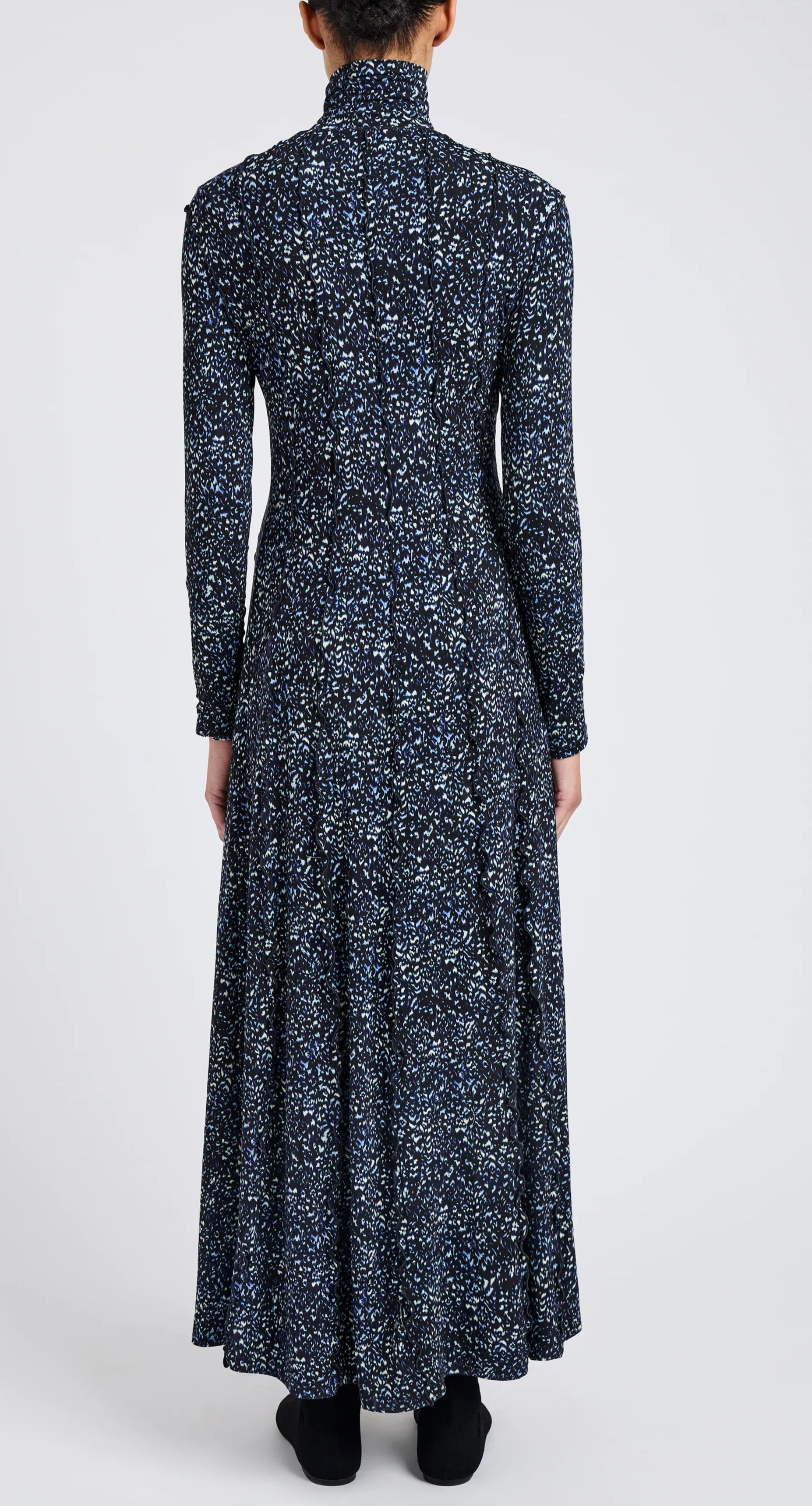 A person wears the Mabel Cheetah Jersey Dress by Proenza Schouler White Label, a long-sleeve, ankle-length dark blue dress with a white and light blue speckled pattern, shown from the back against a plain background.