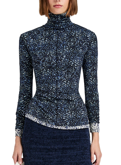 A woman wears the Proenza Schouler White Label Audrey Cheetah Jersey Top, a long-sleeve, turtleneck style with a subtle blue and white pattern, paired with a textured dark skirt. The image is cropped at the shoulders and thighs.