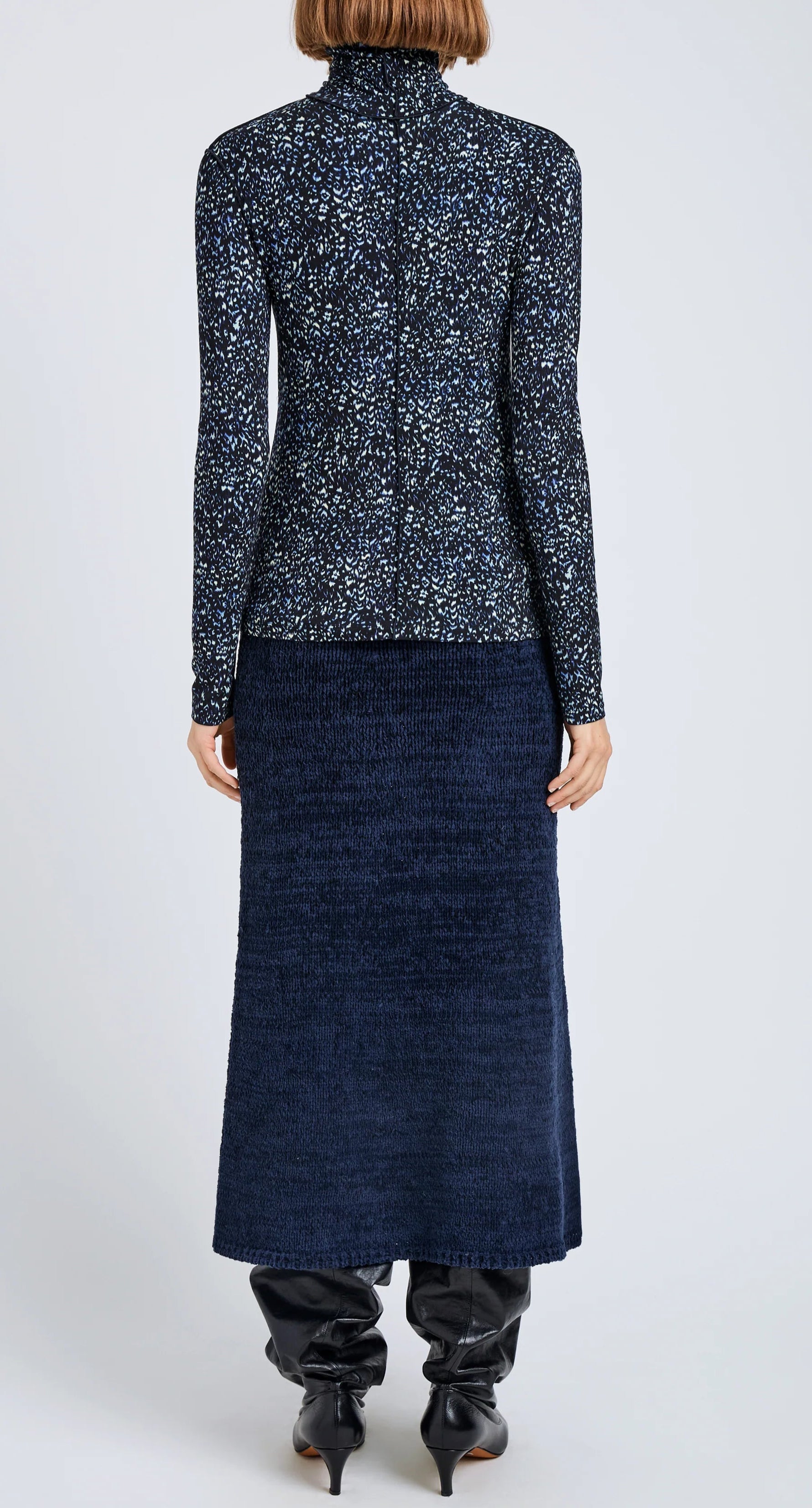 A person stands facing away in the Proenza Schouler White Label Audrey Cheetah Jersey Top, paired with a textured navy midi skirt and black boots against a plain light background.