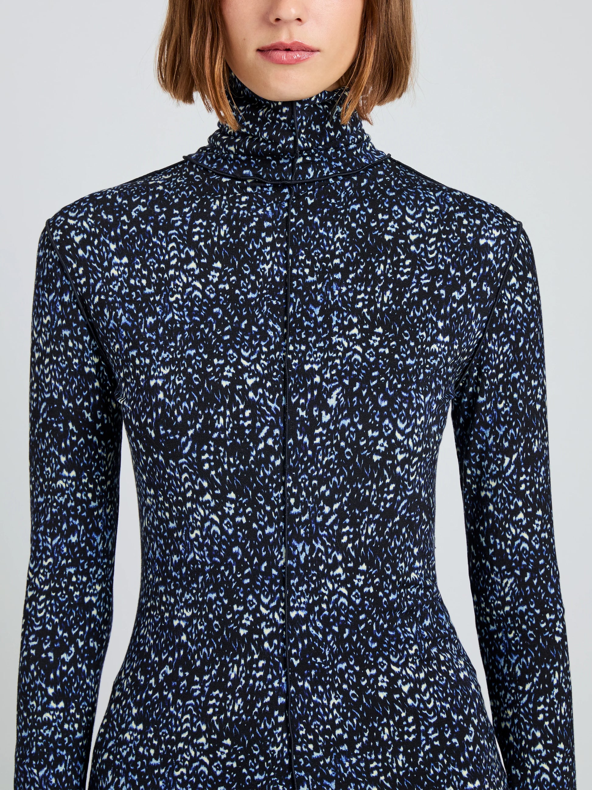 A woman wears the Audrey Cheetah Jersey Top by Proenza Schouler White Label, a long-sleeve, high-neck fitted turtleneck with a blue and white abstract print on black.