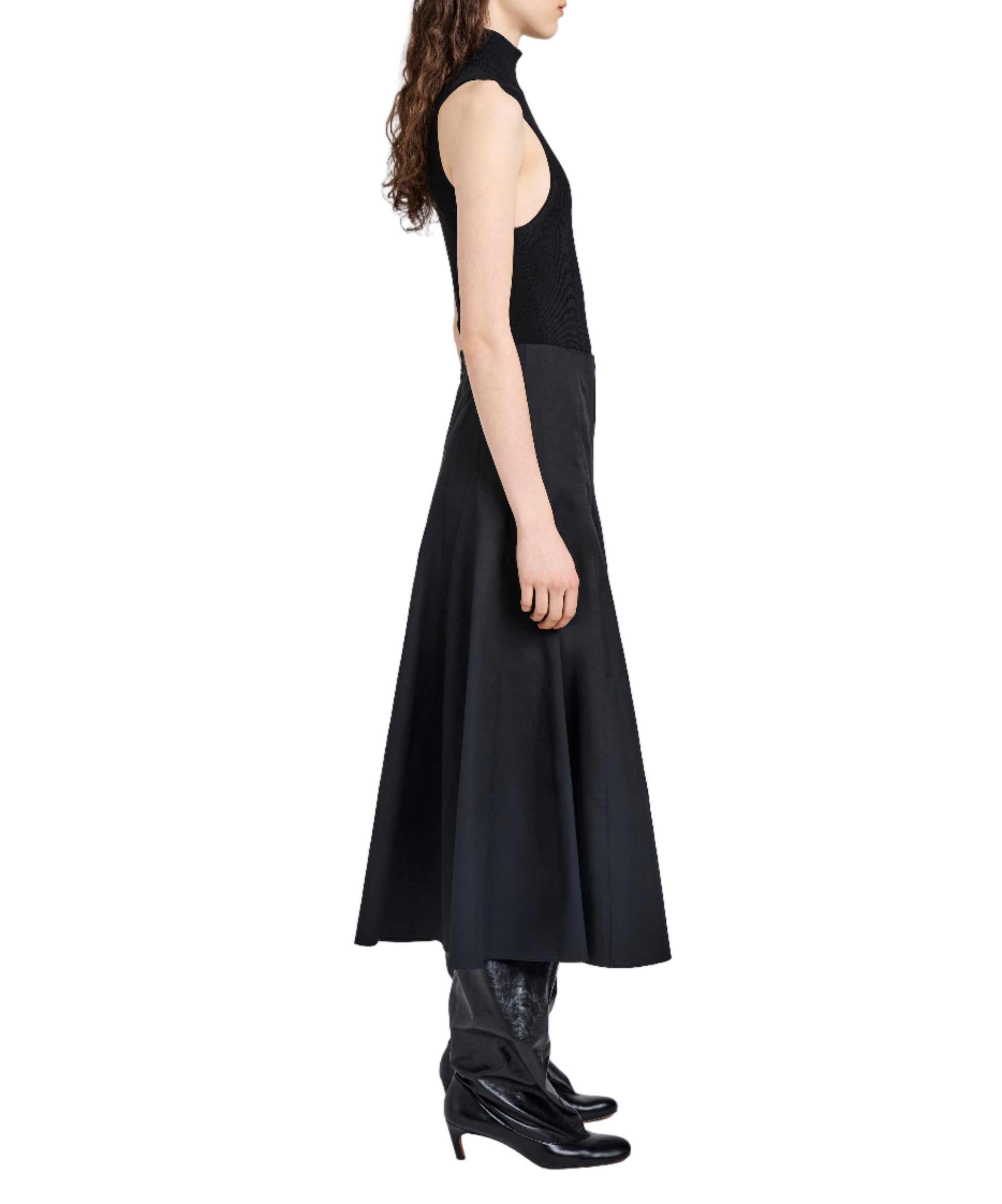A woman in profile wears a sleeveless black top, black boots, and a long A-line Heidi Skirt by Proenza Schouler White Label, standing against a white background.