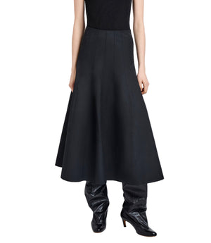 A person wears a black sleeveless top with the Proenza Schouler White Label Heidi Skirt—a high-waisted, flared black A-line skirt in Tech Cotton—paired with black heeled boots, standing against a white background.