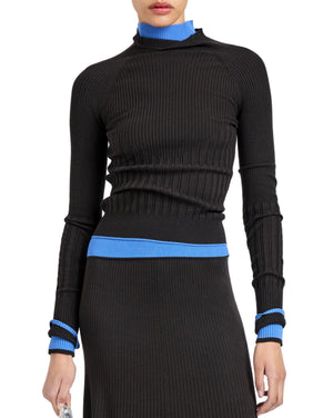 A person wears the Proenza Schouler White Label Daniella Sweater—a ribbed black turtleneck with blue collar, waist, and cuff accents—paired with a matching black skirt.