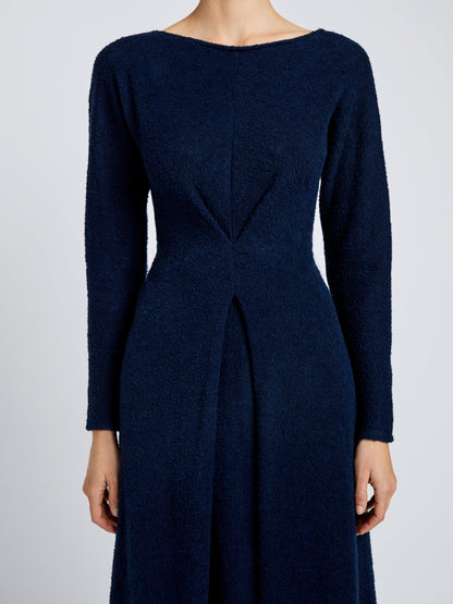 A person wearing the Proenza Schouler White Label Sai Wool Jersey Dress—a long-sleeved, navy blue piece with geometric seams, a fitted waist, and an elegant A-line silhouette.