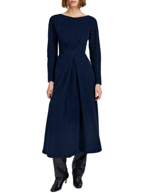 A woman wears the Sai Wool Jersey Dress by Proenza Schouler White Label—a navy, long-sleeved, ankle-length dress with pleats and an A-line silhouette—paired with black heeled boots.