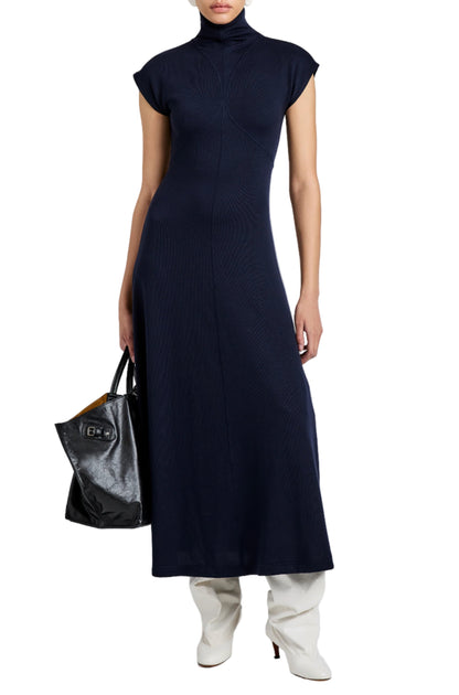 Person wearing a navy blue Proenza Schouler White Label Brea Brushed Rib Dress with an A-line silhouette, high neck, and short sleeves, styled with white boots and a large black handbag.