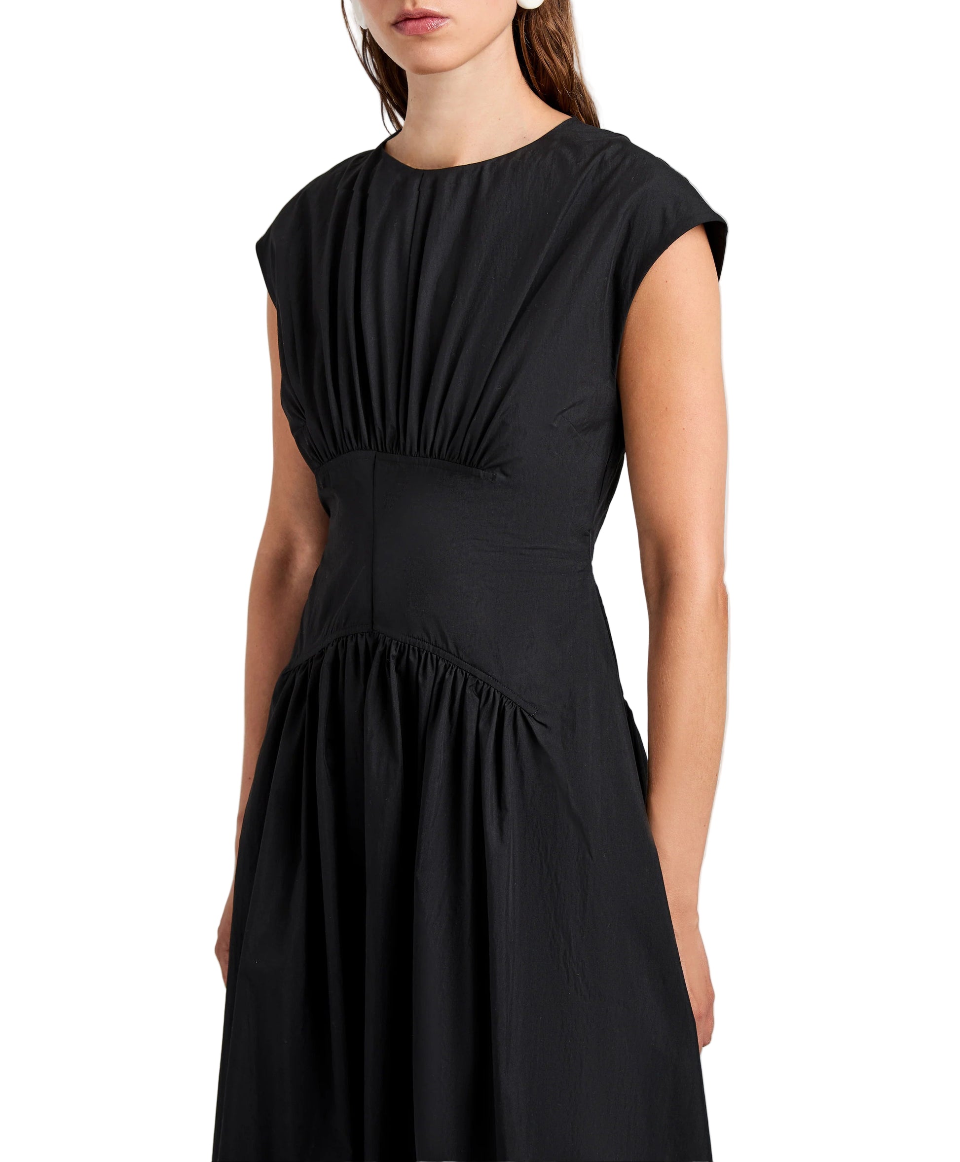 A woman wears the Nyssa Dress by Proenza Schouler White Label—a black Tech Cotton dress with shirred short sleeves, fitted bodice, and A-line silhouette—standing against a plain light background.