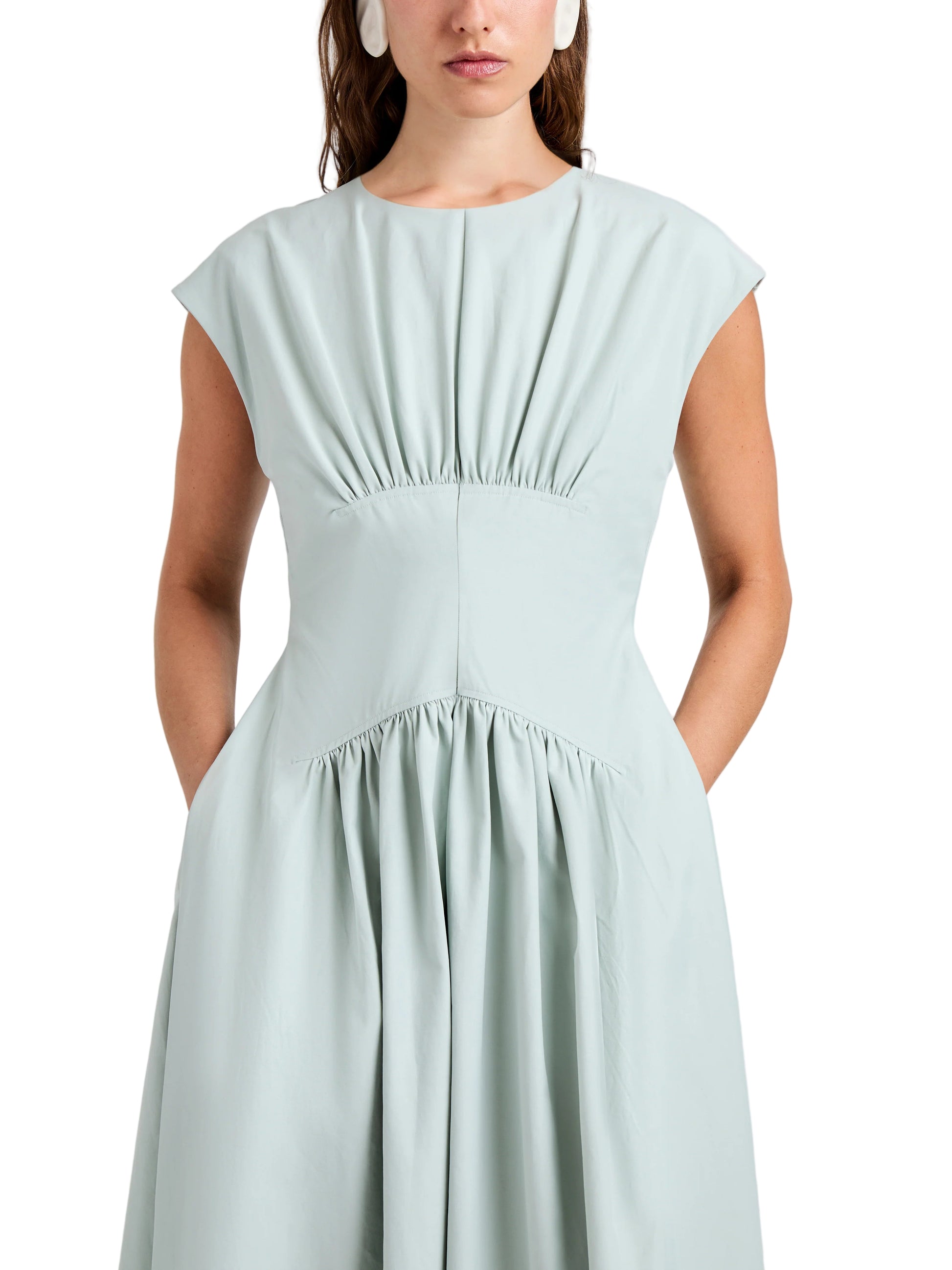 A woman wears the Proenza Schouler White Label Nyssa Dress in light blue tech cotton, featuring front shirring and pockets, shown from shoulders to knees against a plain backdrop.