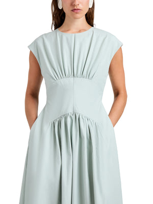A woman wears the Proenza Schouler White Label Nyssa Dress in light blue tech cotton, featuring front shirring and pockets, shown from shoulders to knees against a plain backdrop.