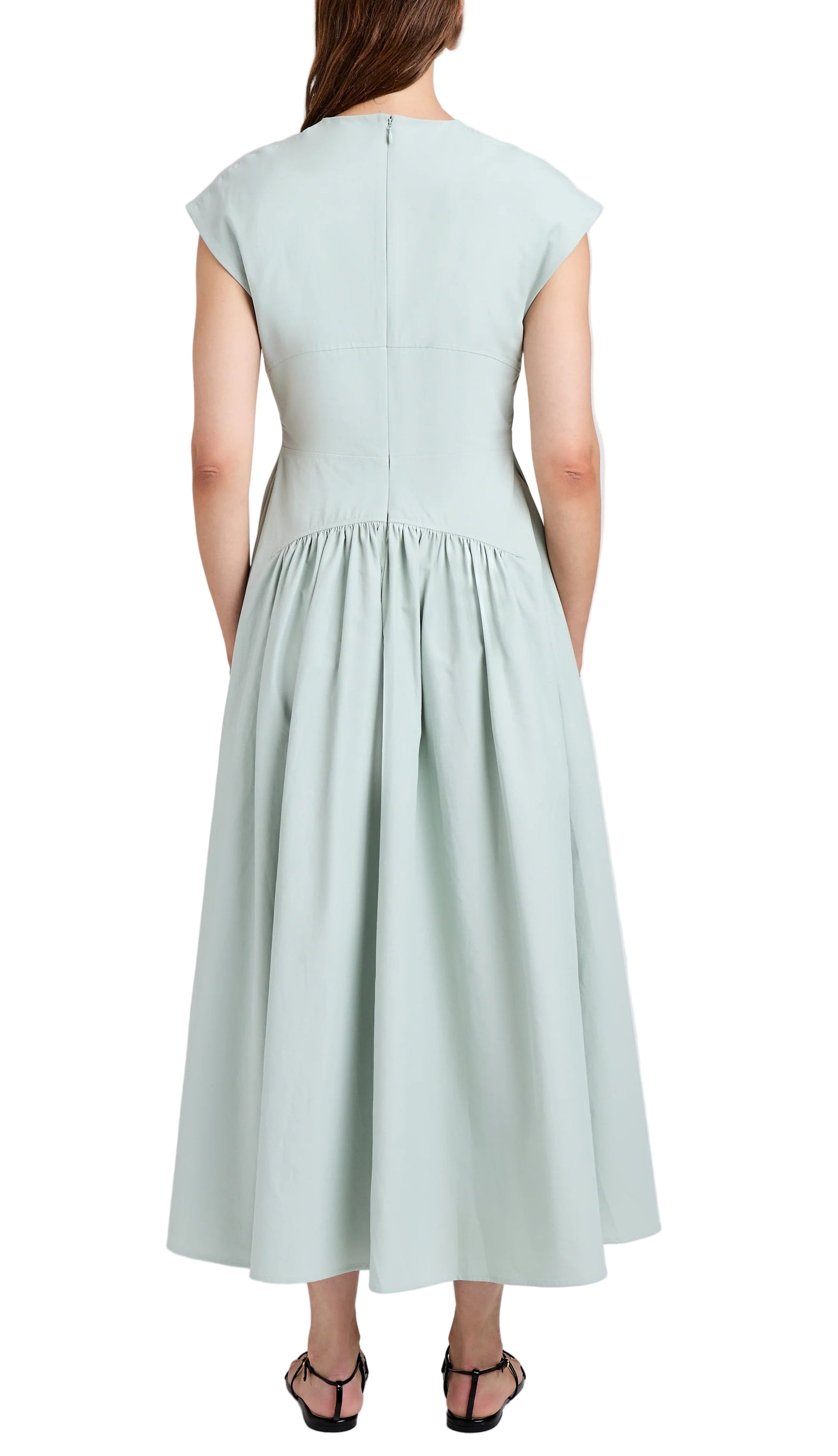 A person is seen from the back wearing the Nyssa Dress by Proenza Schouler White Label—a light green, short-sleeved, midi A-line with shirring at the gathered waist—paired with black sandals.