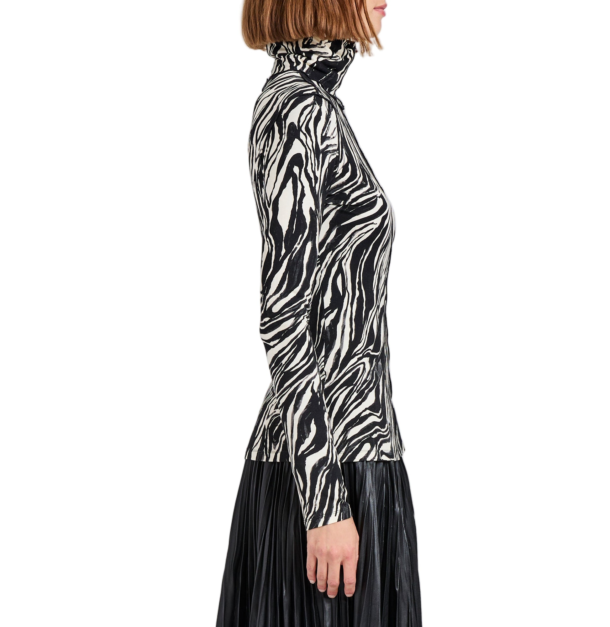 A woman, shown from the side, wears the Audrey Marble Jersey Top by Proenza Schouler White Label—a slim, long-sleeve turtleneck with a black-and-white print—paired with a black pleated skirt.