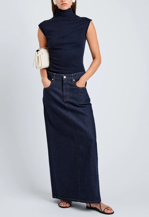 A woman wears the Zane Brushed Rib Top by Proenza Schouler White Label, a dark denim maxi skirt, black sandals, and carries a small beige handbag.