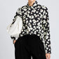 Person wearing a black and white floral print Proenza Schouler White Label Ansel Top, black pants, and holding a large white bag under their arm.
