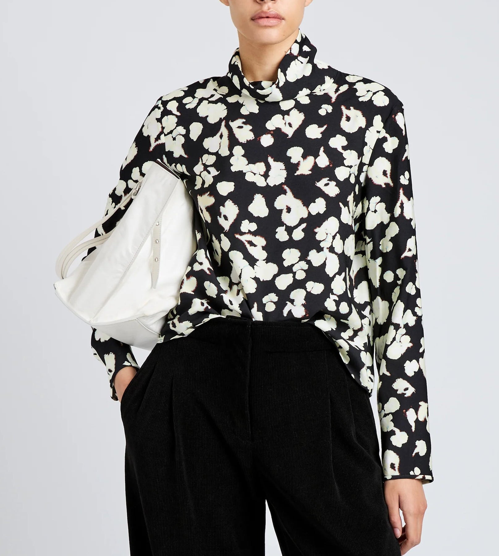 Person wearing a black and white floral print Proenza Schouler White Label Ansel Top, black pants, and holding a large white bag under their arm.