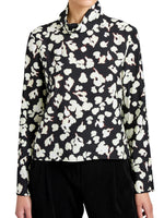 Wearing the Ansel Top by Proenza Schouler White Label—a long-sleeve black blouse with a white floral print, made from soft twill and featuring a high neckline.