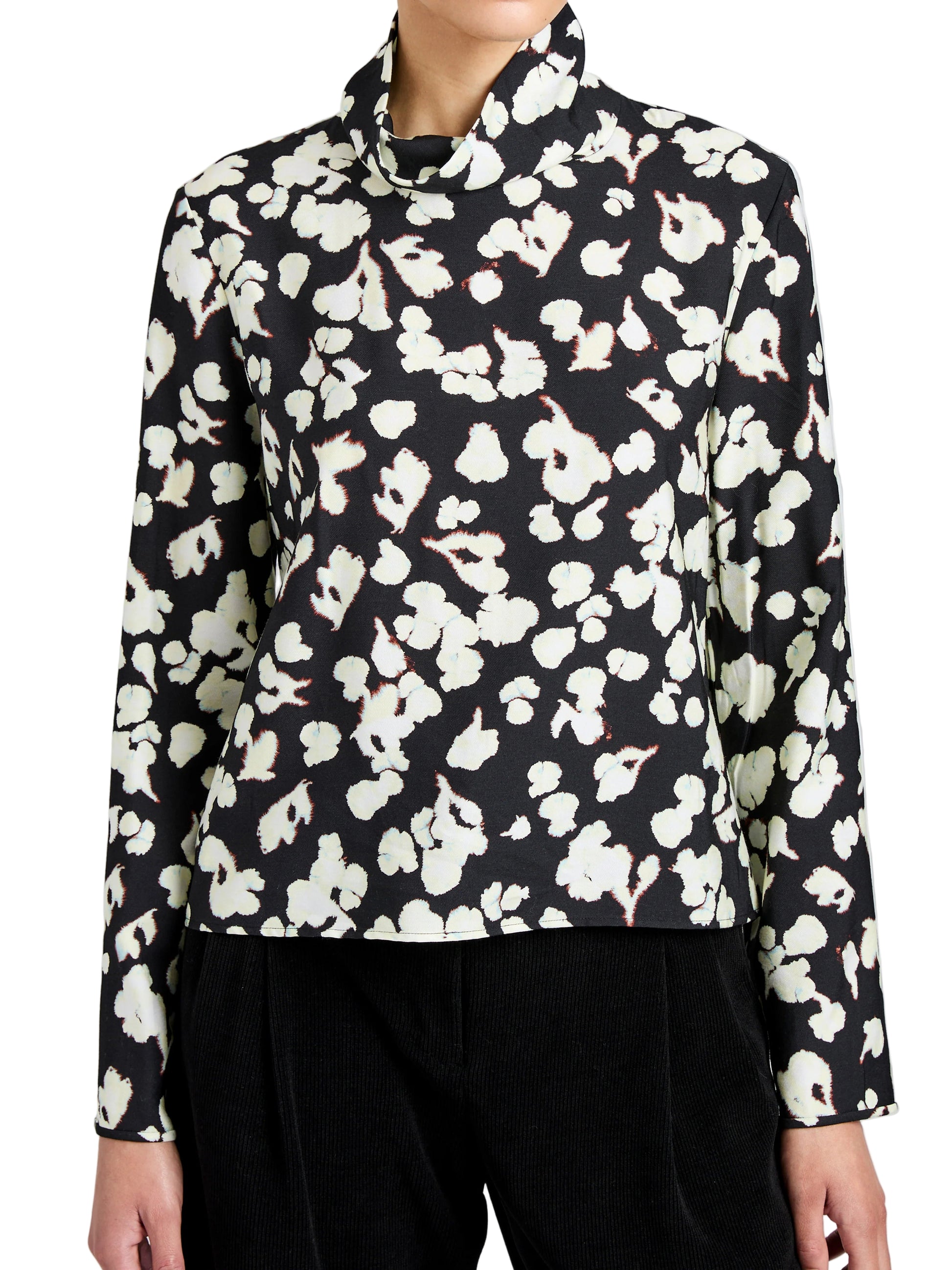 Wearing the Ansel Top by Proenza Schouler White Label—a long-sleeve black blouse with a white floral print, made from soft twill and featuring a high neckline.