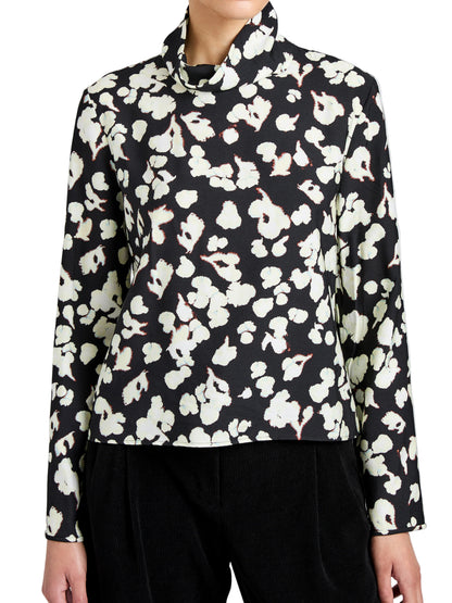 Wearing the Ansel Top by Proenza Schouler White Label—a long-sleeve black blouse with a white floral print, made from soft twill and featuring a high neckline.