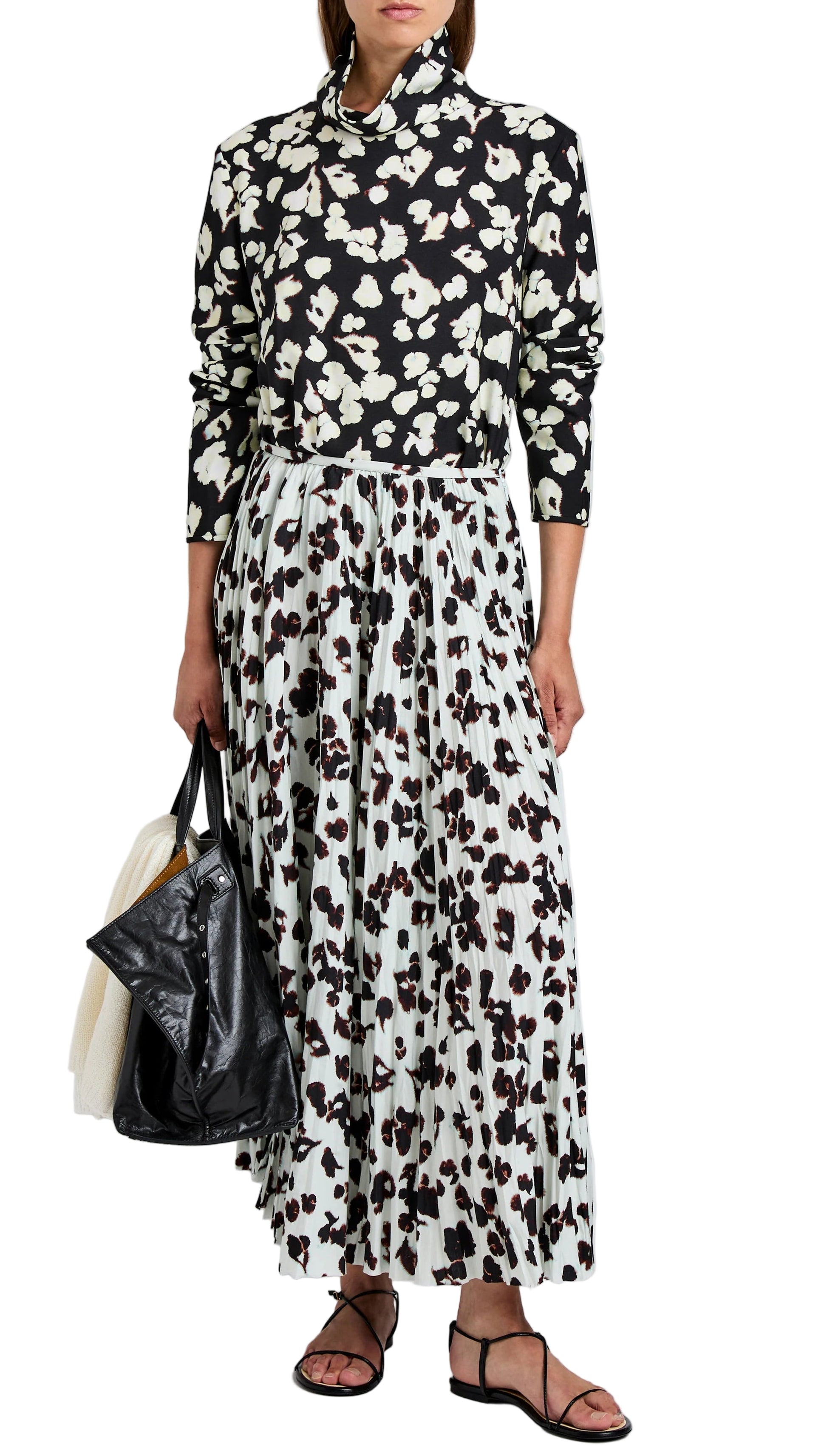 A person wears the Proenza Schouler White Label Runa Skirt—a black and white floral A-line design in soft twill with pleats—paired with a long-sleeve top, black bag, and black sandals.
