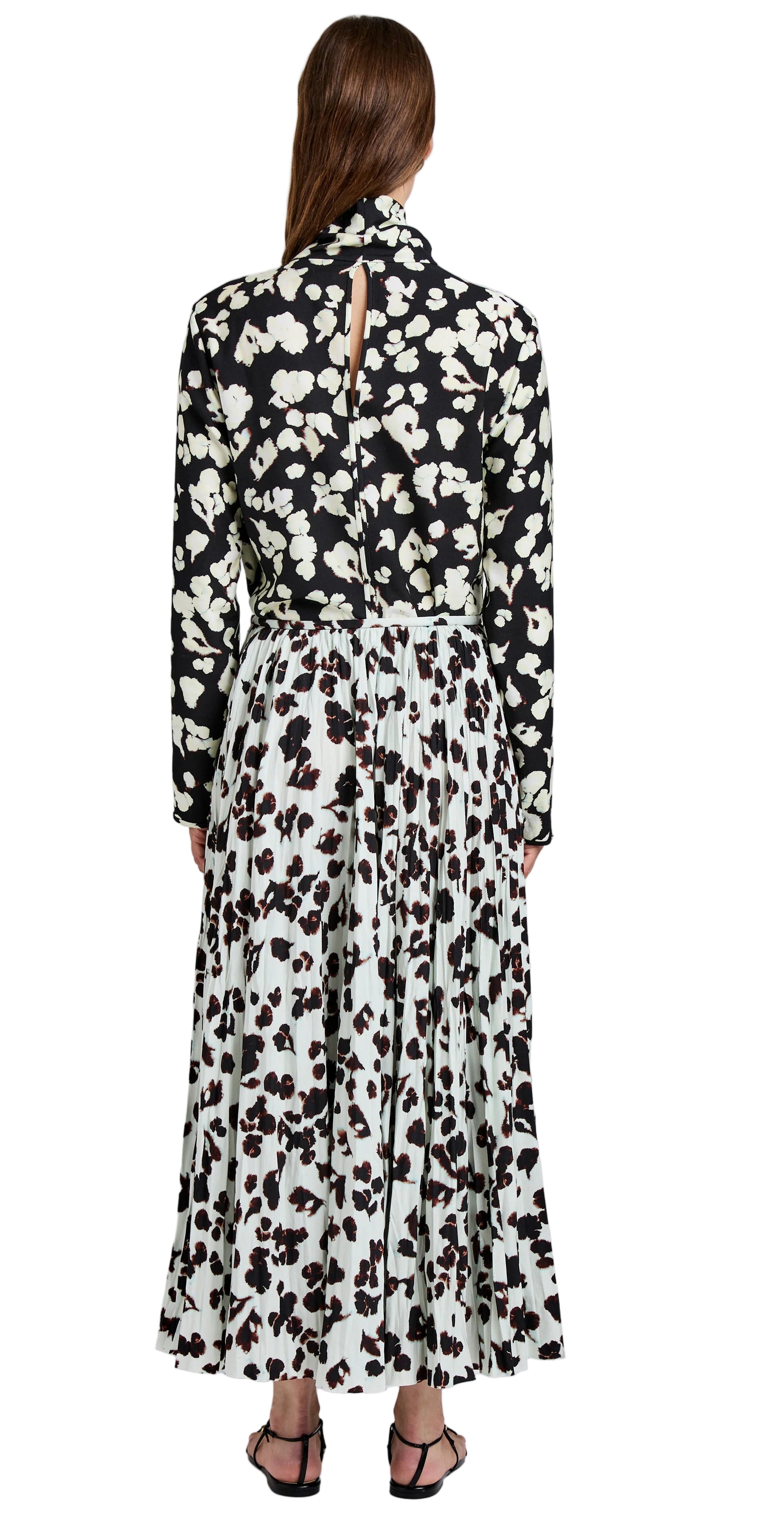 A woman stands facing away, wearing the Runa Skirt by Proenza Schouler White Label—a black and white floral print skirt in soft twill with a pleated A-line silhouette—paired with black sandals.