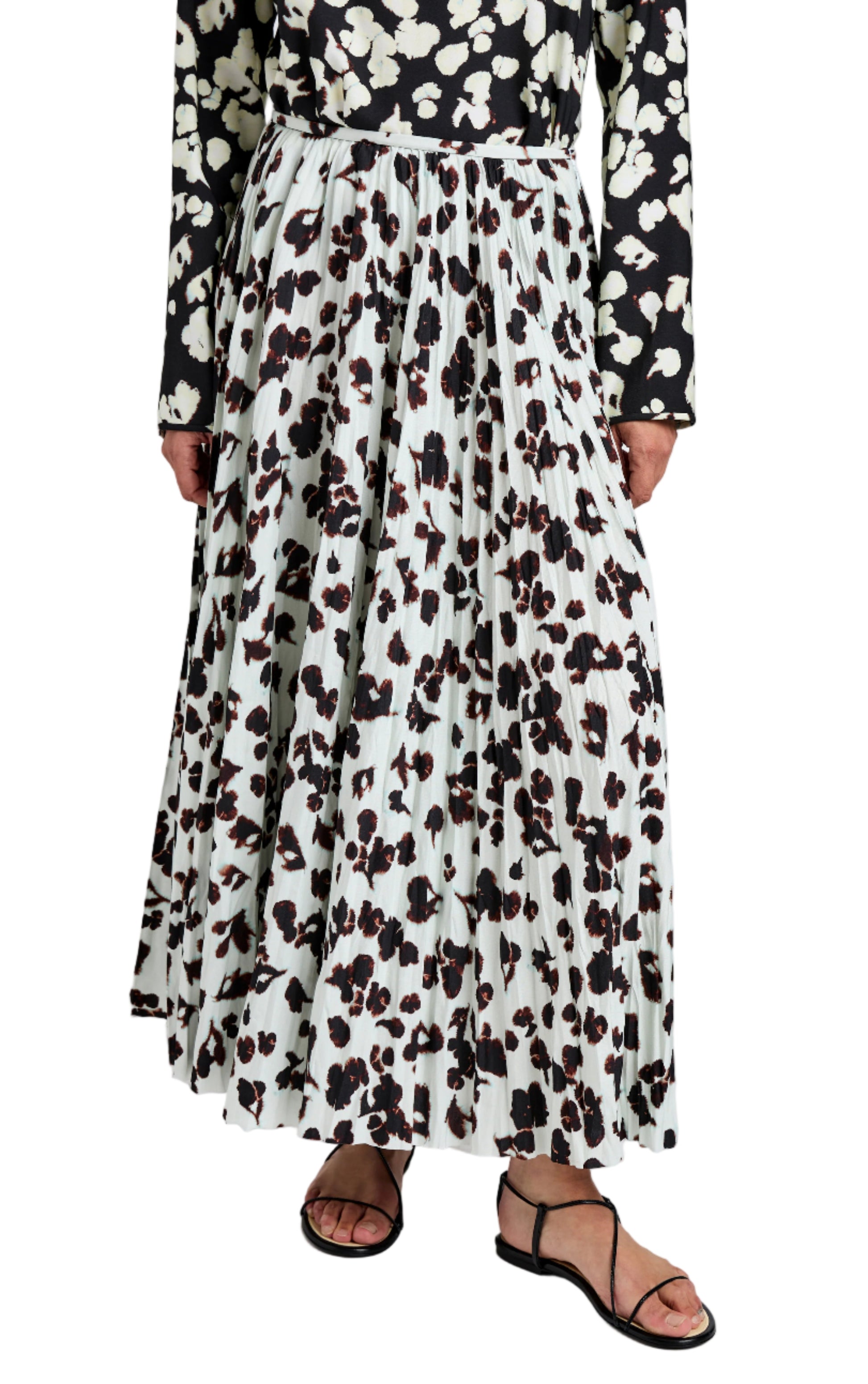 A person wears the Proenza Schouler White Label Runa Skirt, an A-line floral print skirt with black and brown abstract patterns, styled with a black and white patterned top and black sandals.