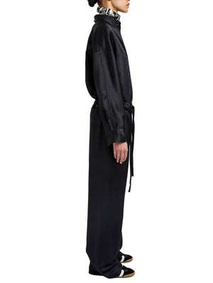 A woman in profile wears the Proenza Schouler White Label Magnus Crinkled Crepe Pant—long, black, high-waisted, wide-leg—with a belted waist, black and white shoes, and a patterned scarf or collar.