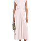 A person wears the sleeveless, light pink Miranda Dress by Proenza Schouler White Label, featuring a twisted front detail and A-line silhouette, paired with a green handbag and black sandals.