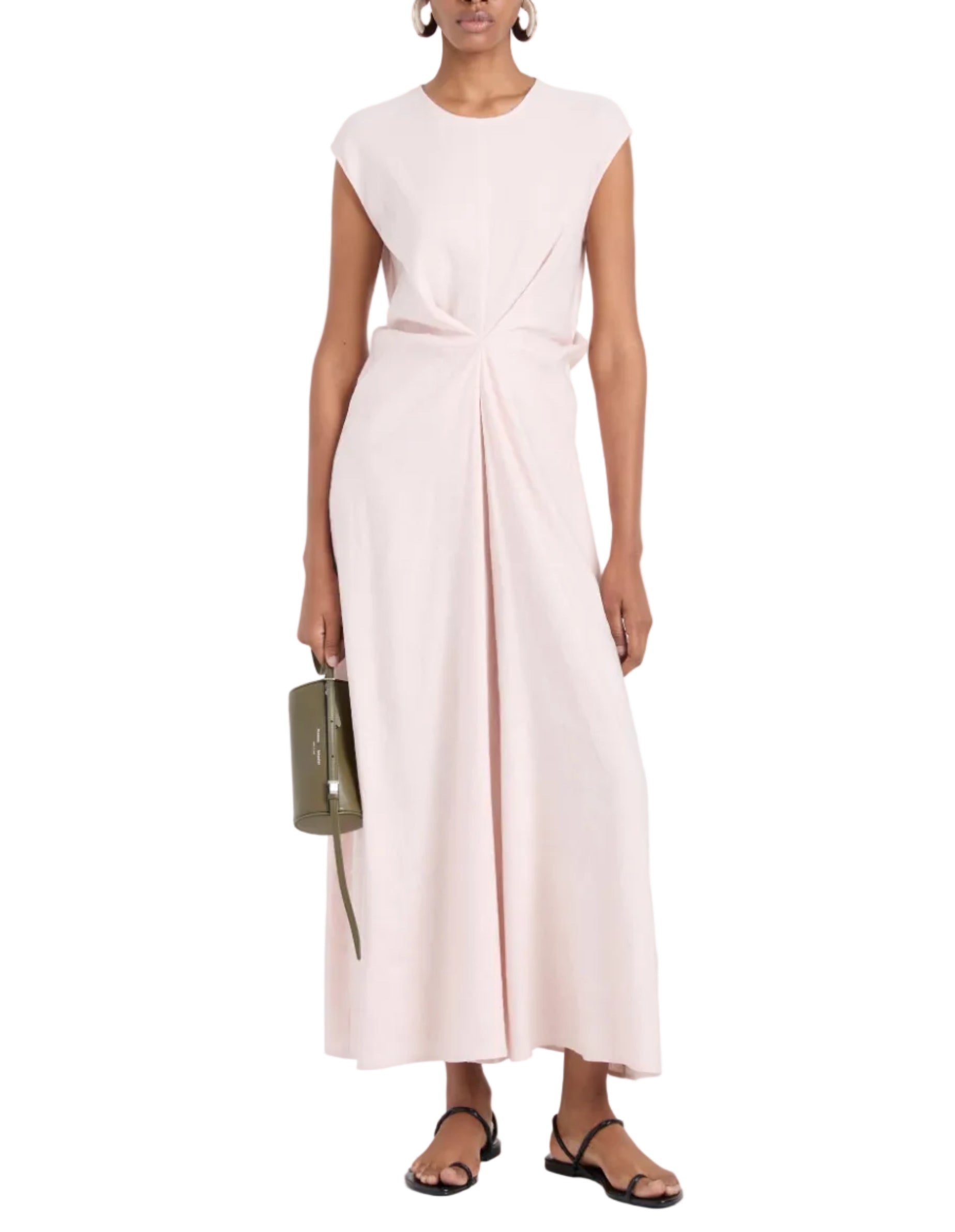A person wears the sleeveless, light pink Miranda Dress by Proenza Schouler White Label, featuring a twisted front detail and A-line silhouette, paired with a green handbag and black sandals.