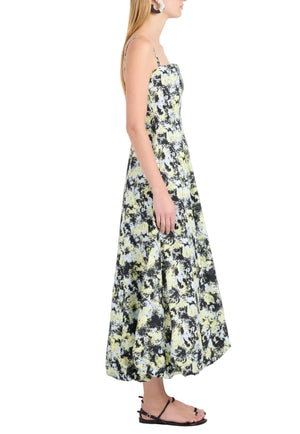 A woman stands in profile wearing the Proenza Schouler White Label Tulah Dress, a sleeveless, ankle-length floral piece with thin straps, styled with black flat sandals and statement round earrings.