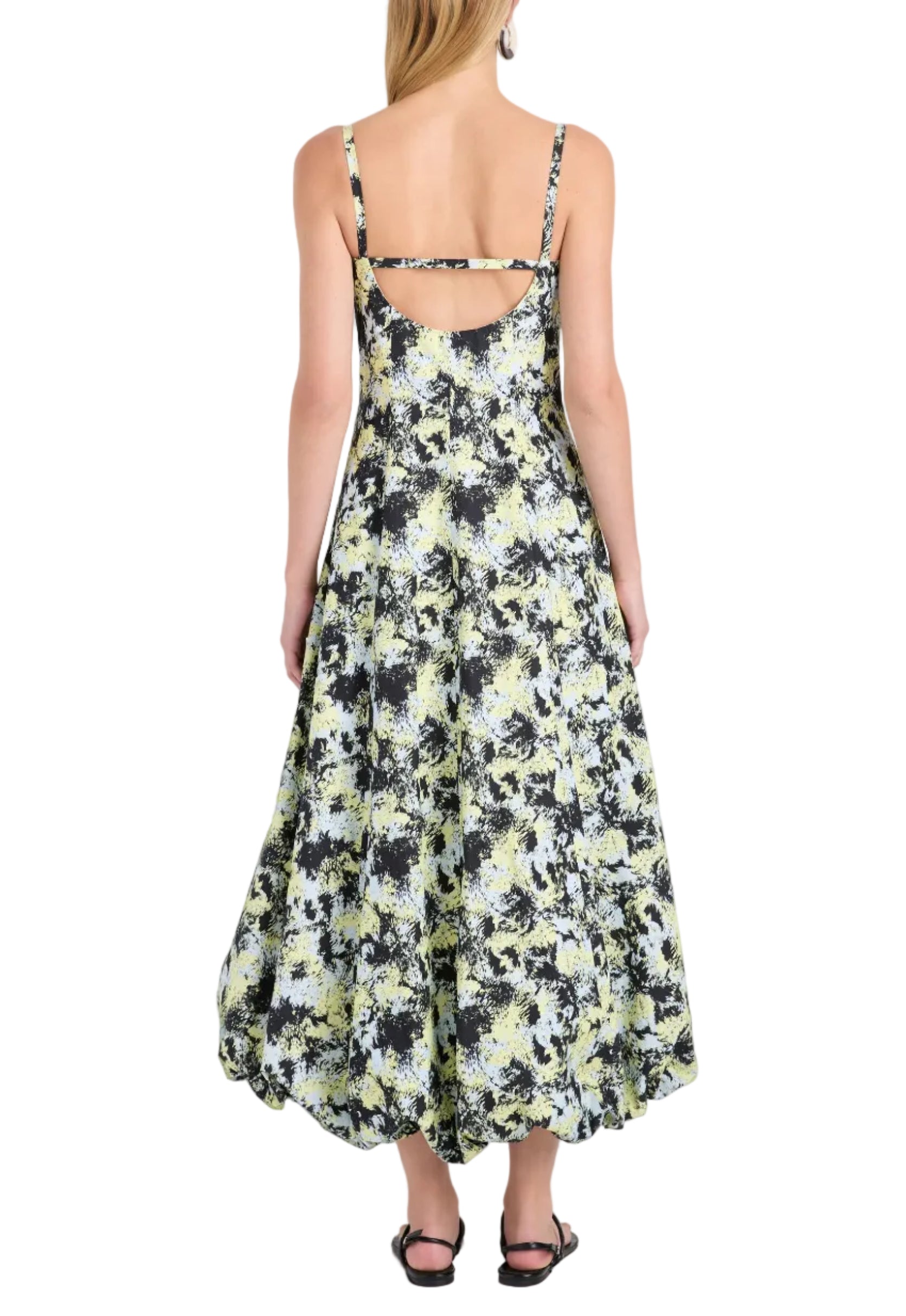 A woman is shown from the back wearing the Tulah Dress by Proenza Schouler White Label, a sleeveless fit-and-flare floral print dress in black, white, and yellow hues with spaghetti straps, paired with black sandals.