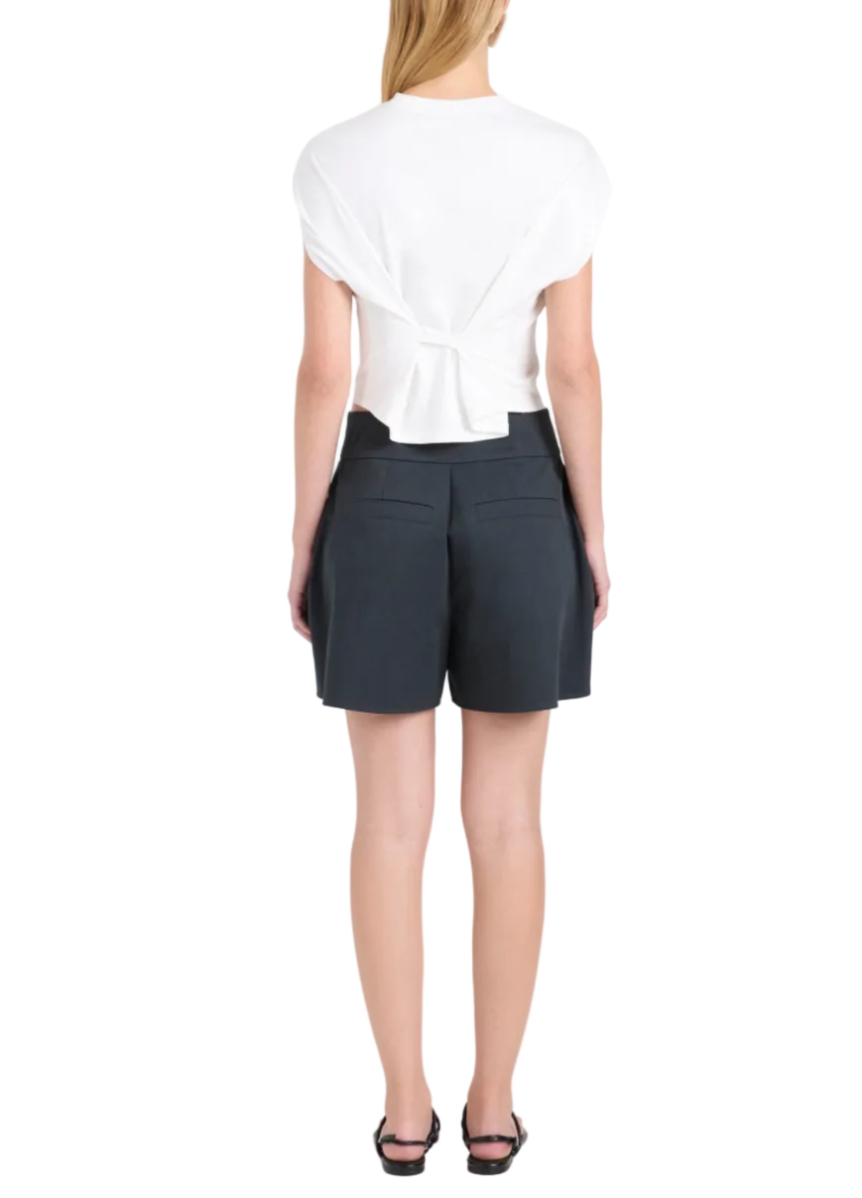 A woman faces away, wearing a white knotted-back top, Proenza Schouler White Label's Natalia Short, and black sandals against a plain white background.