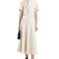 Woman in a short-sleeve cream Proenza Schouler White Label Elizabeth Dress with tie belt, styled with black sandals and a small black bag, standing against a white background.
