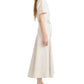 Woman in a short-sleeve, belted Elizabeth Dress by Proenza Schouler White Label, crafted from cream cotton linen with a fit-and-flare silhouette, paired with black sandals and standing in profile against a white background.