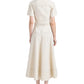 A woman faces away, wearing a Proenza Schouler White Label Elizabeth Dress in cotton linen with short sleeves and black sandals, set against a white background.