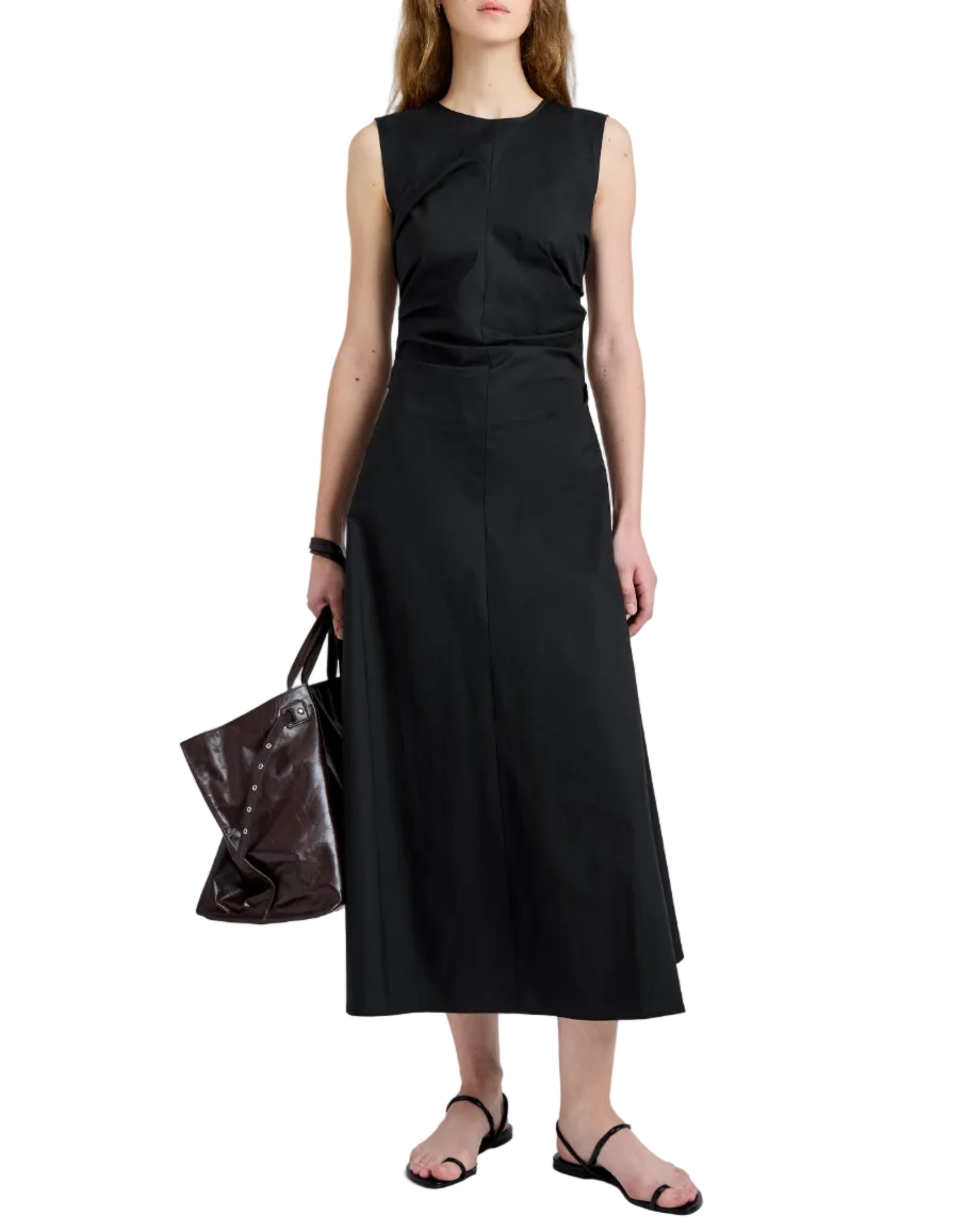 A person wears the Proenza Schouler White Label Anoushka Dress—sleeveless, black with an abstract brushstroke print—paired with black sandals and carrying a large black handbag by their side.