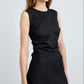 A woman in the sleeveless black Anoushka Dress by Proenza Schouler White Label stands against a plain light background, her arms relaxed at her sides.