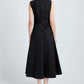 A woman, facing away, wears the Anoushka Dress by Proenza Schouler White Label—a sleeveless black poplin dress featuring a fitted bodice, flared skirt, back zipper, and subtle ruching—paired with black sandals.