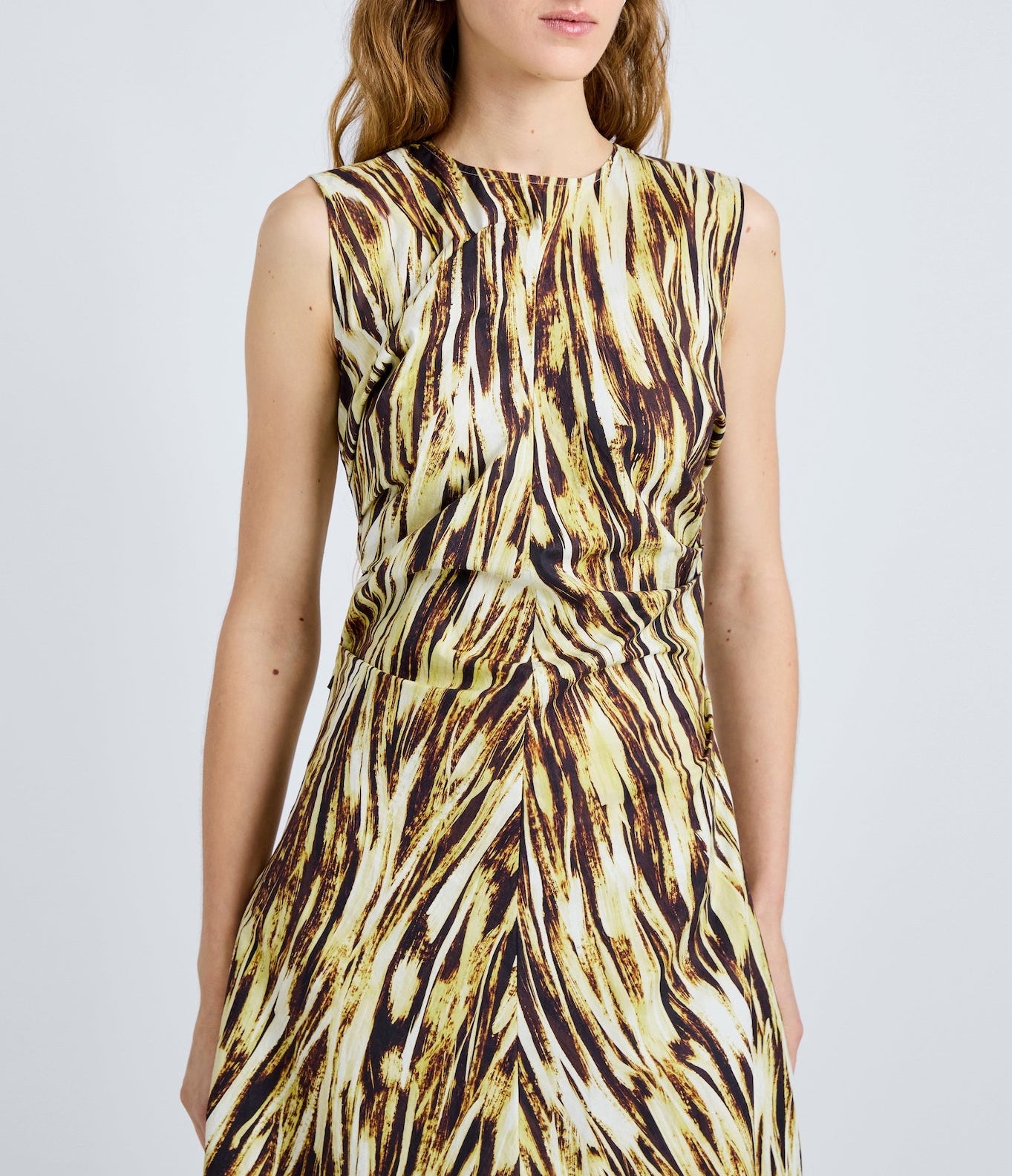 A woman wears the Anoushka Dress by Proenza Schouler White Label, a sleeveless poplin dress with yellow, brown, and black abstract brushstroke print, standing against a plain light background.