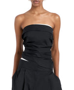 A person shown from shoulders to hips wears the Maisy Strapless Top by Proenza Schouler White Label, a black poplin top with white trim, paired with matching black high-waisted pleated pants.