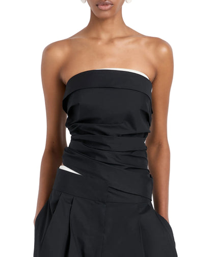 A person shown from shoulders to hips wears the Maisy Strapless Top by Proenza Schouler White Label, a black poplin top with white trim, paired with matching black high-waisted pleated pants.