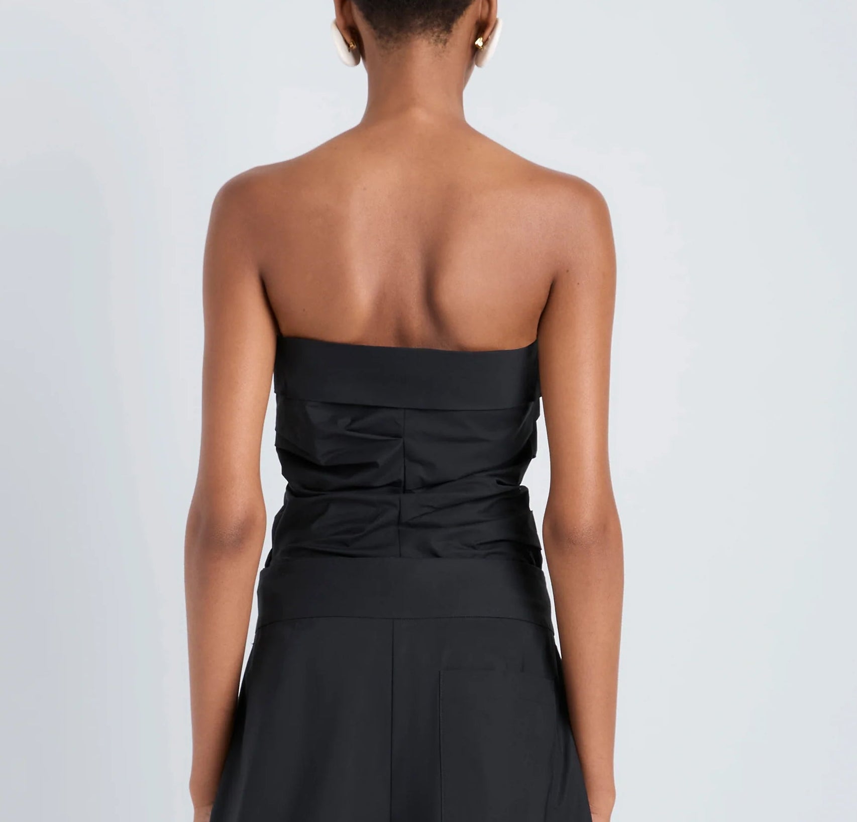 Person shown from the back wearing the Maisy Strapless Top by Proenza Schouler White Label and black pants, with short hair and gold hoop earrings, set against a plain background.