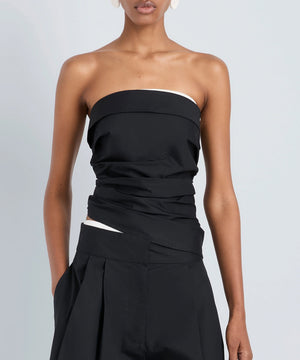 A person wearing the Maisy Strapless Top by Proenza Schouler White Label with black high-waisted pants, standing against a plain light gray background.