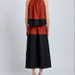 Person stands facing away, wearing the Esme Top by Proenza Schouler White Label in rust and black with a cropped silhouette, paired with black sandals, against a plain light gray background.